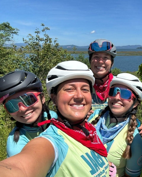 Four cyclists in helmets taking a selfie by the water